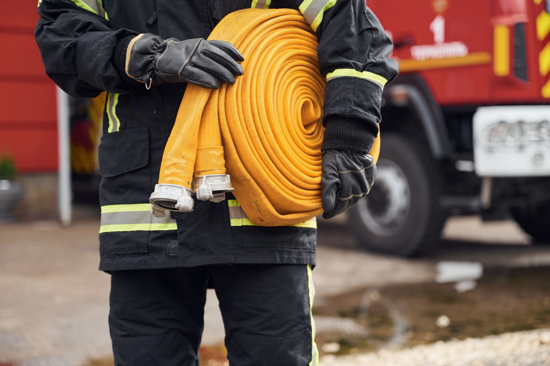 Outside near truck and with fire hose in hands. Woman in uniform is at work in department